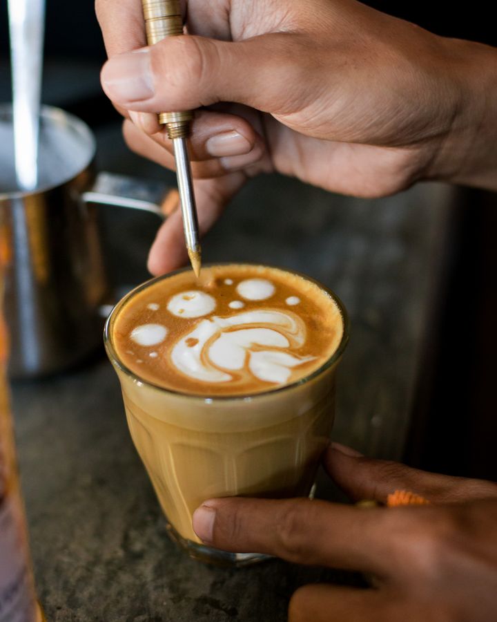 A barista finishing the latte art on a glass of espresso and milk