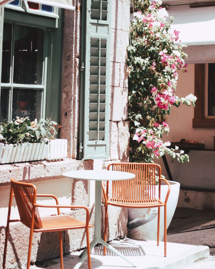 Sunlit patio table and chairs beside the cafe window under flowering vines