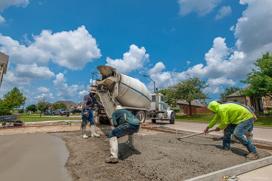 A three person crew raking wet concrete off a mixer truck chute into a formed driveway slab