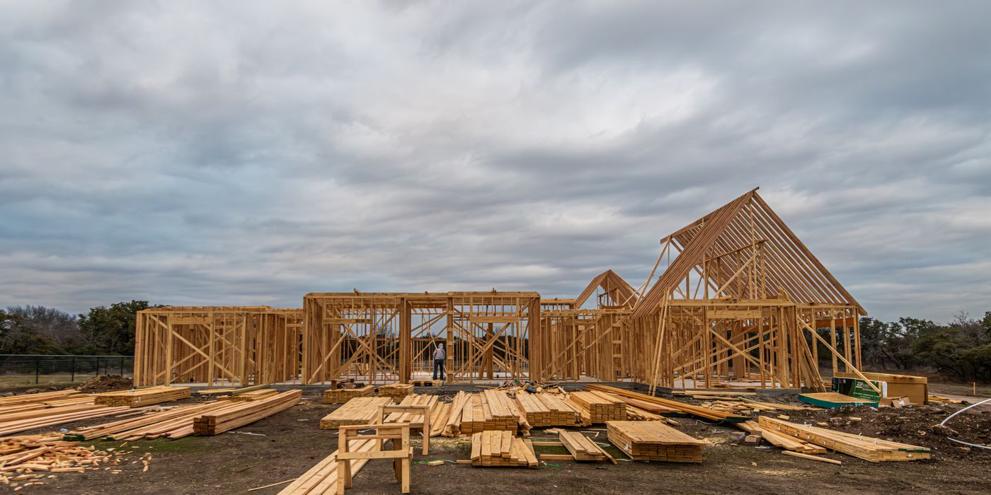 A custom home at framing stage, roof trusses set over the great room with framing timber stacked on the pad