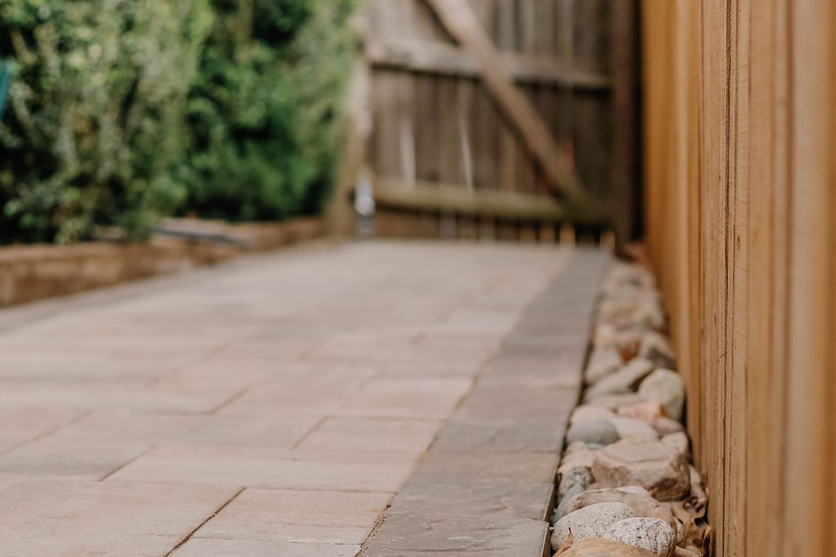 Wide flagstone walk with a river cobble drainage edge along a fence