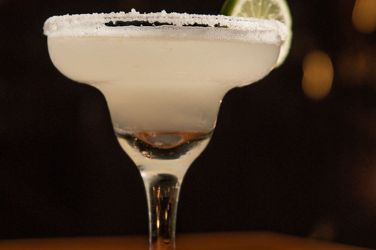 Salt rimmed margarita with a lime wheel on the dark bar