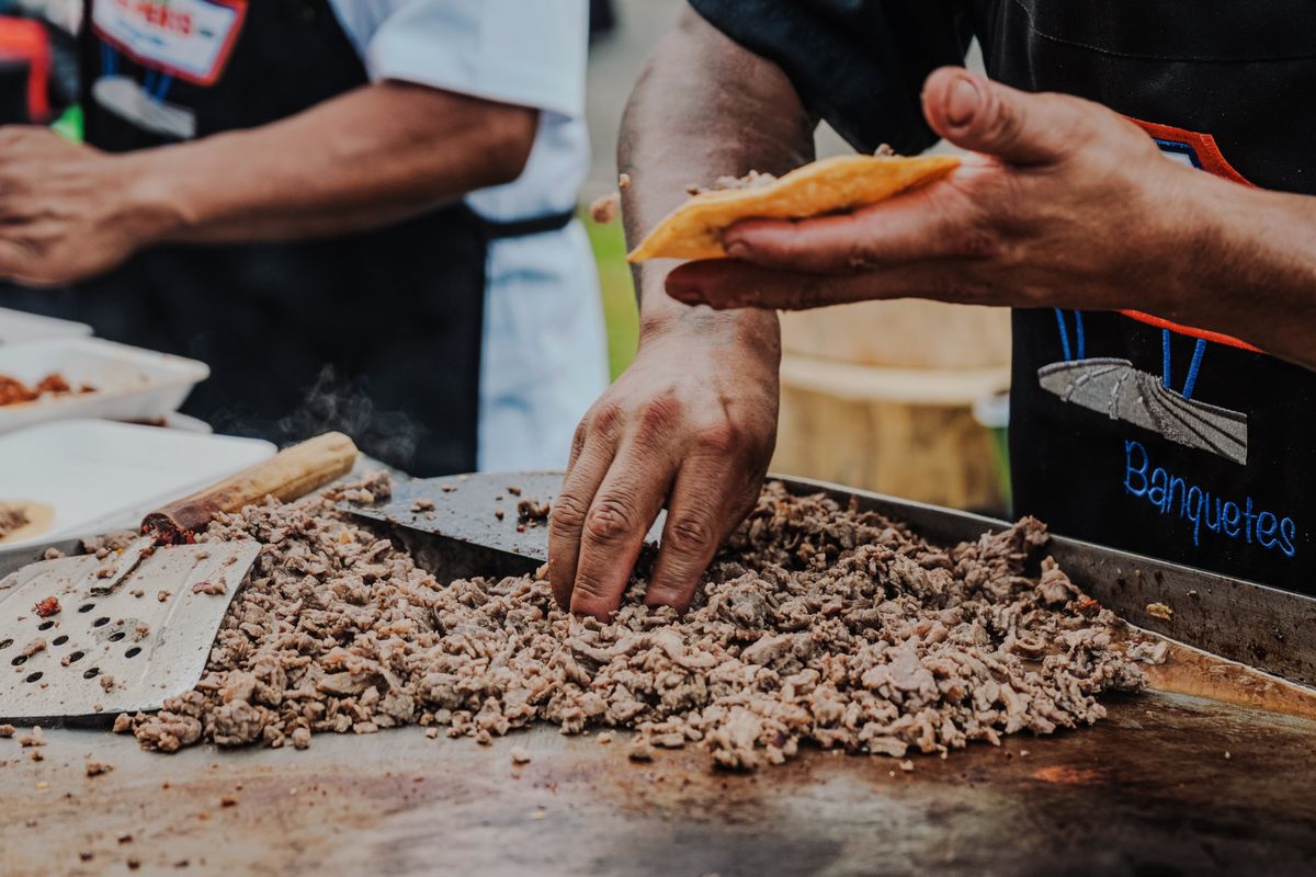 Cook building tacos off a hot plancha at a catered taco bar