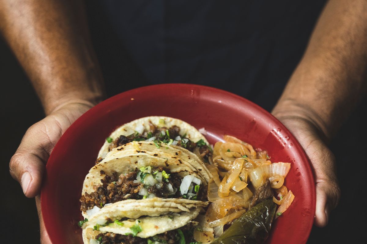Three street tacos with onion and cilantro on a red plate