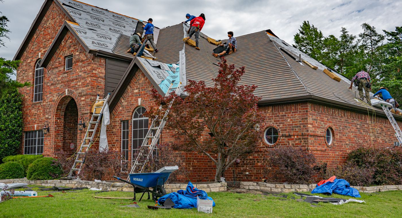 A roofing crew stripping and re-laying shingles on a two storey brick house