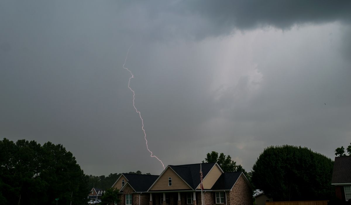 A storm cell over a suburban street with lightning striking behind the rooflines